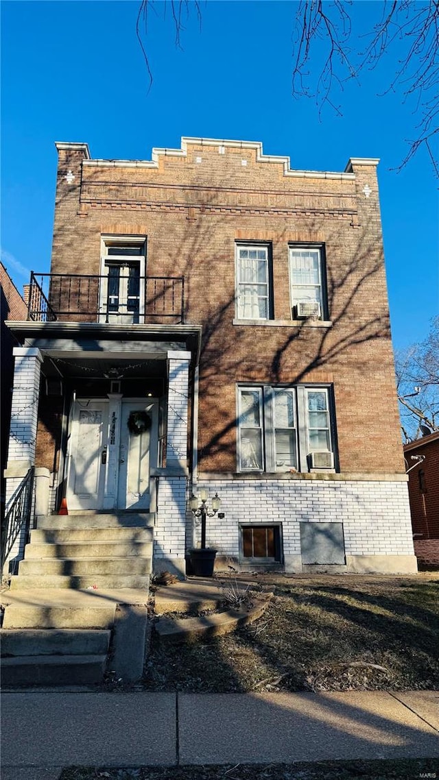 view of front facade featuring cooling unit, brick siding, and a balcony