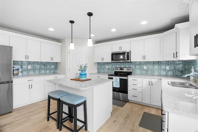 kitchen featuring decorative light fixtures, appliances with stainless steel finishes, white cabinetry, a sink, and a kitchen island