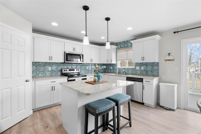 kitchen featuring stainless steel appliances, a kitchen island, decorative light fixtures, and white cabinets