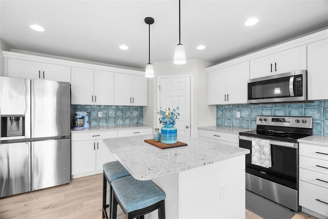 kitchen featuring a center island, decorative light fixtures, appliances with stainless steel finishes, light wood-style floors, and white cabinetry