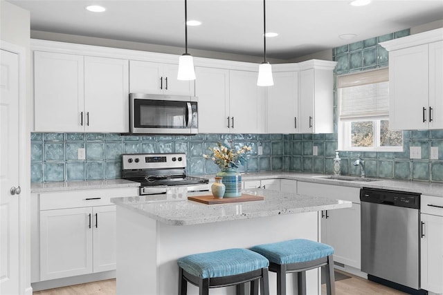 kitchen with appliances with stainless steel finishes, white cabinets, a sink, and a center island