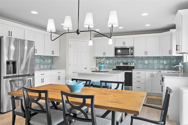 kitchen with a center island, stainless steel appliances, white cabinetry, pendant lighting, and a sink