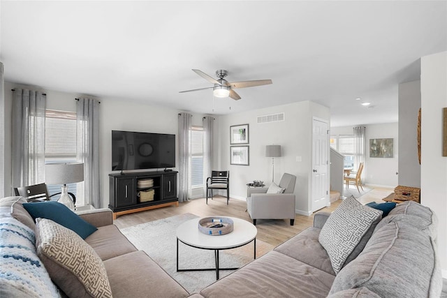 living room with light wood-type flooring, ceiling fan, visible vents, and baseboards