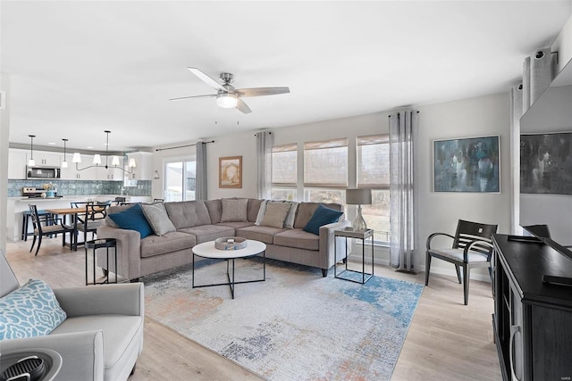 living room featuring ceiling fan with notable chandelier, light wood finished floors, and baseboards