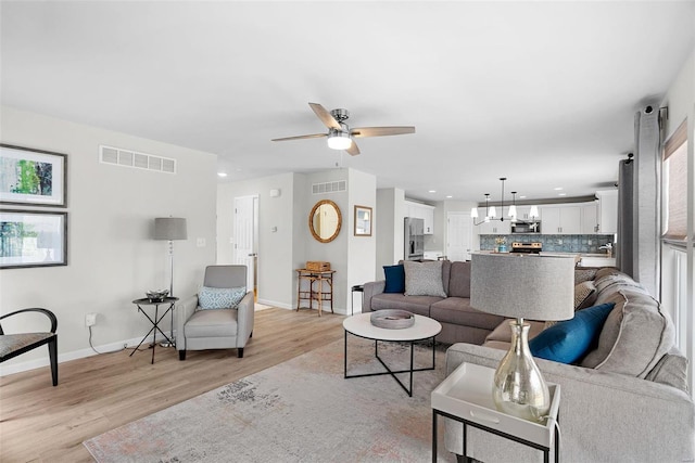 living room featuring light wood-type flooring, visible vents, baseboards, and recessed lighting