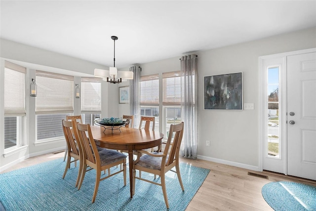 dining space featuring a healthy amount of sunlight, a notable chandelier, light wood-style flooring, and baseboards