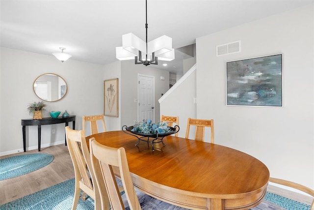 dining room featuring baseboards, visible vents, wood finished floors, stairs, and a chandelier