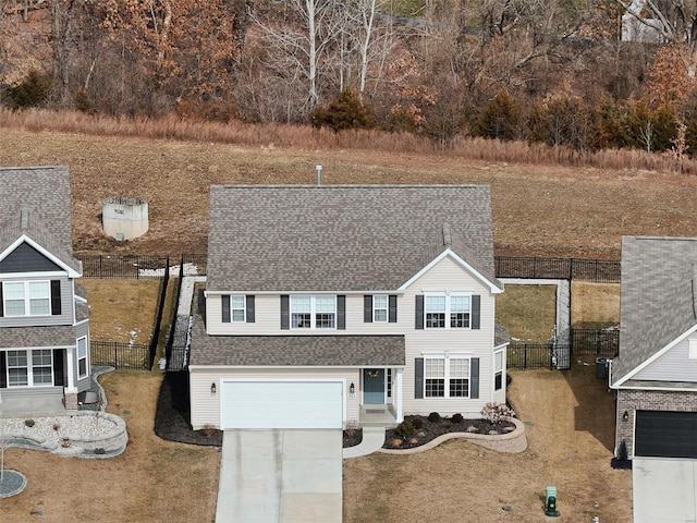 traditional-style house featuring driveway, an attached garage, fence, and a front yard