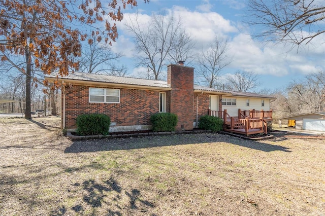 rear view of property featuring a deck, metal roof, brick siding, a yard, and a chimney