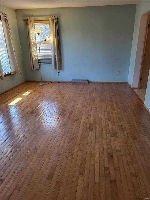 empty room featuring wood-type flooring and a baseboard heating unit