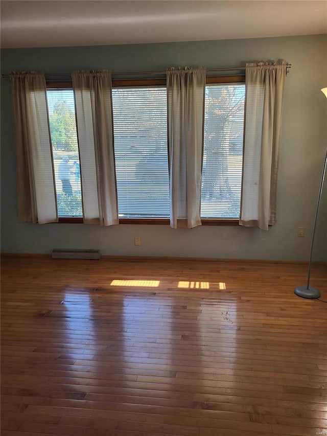 empty room featuring hardwood / wood-style flooring and a baseboard heating unit