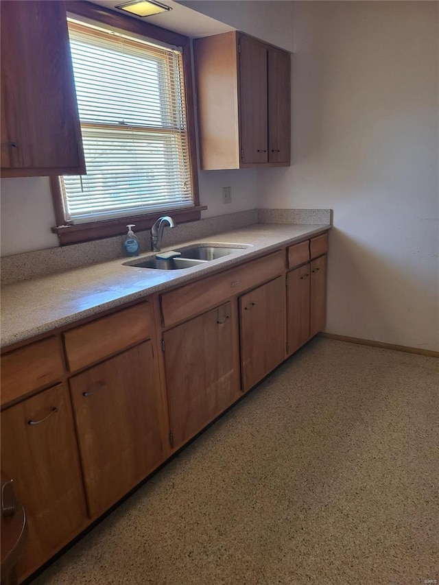 kitchen with brown cabinets, light countertops, a sink, and baseboards