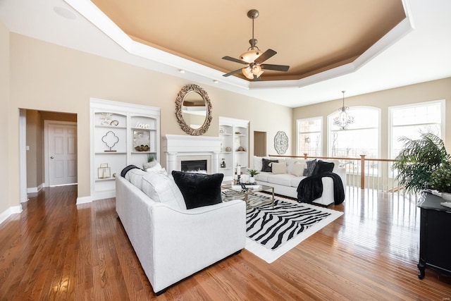 living room featuring baseboards, ceiling fan with notable chandelier, a fireplace, wood finished floors, and a raised ceiling