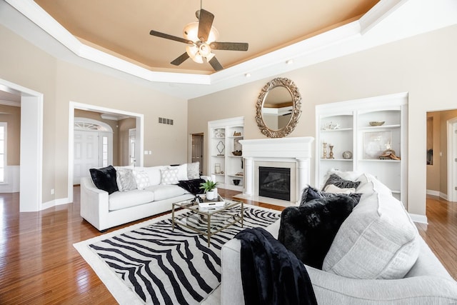 living area with light wood-type flooring, a tray ceiling, a fireplace with flush hearth, and a ceiling fan