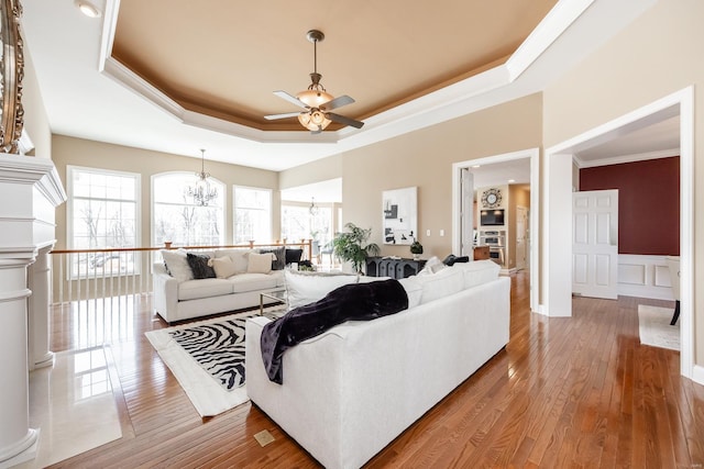 living area featuring crown molding, a wainscoted wall, a tray ceiling, hardwood / wood-style floors, and ceiling fan with notable chandelier