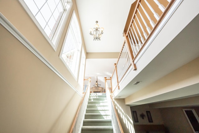 stairway with visible vents, ceiling fan with notable chandelier, and a towering ceiling