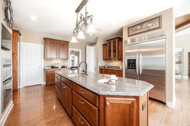 kitchen with a sink, brown cabinetry, a center island with sink, and stainless steel appliances