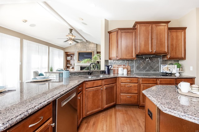 kitchen with light stone countertops, brown cabinets, stainless steel dishwasher, a ceiling fan, and a sink