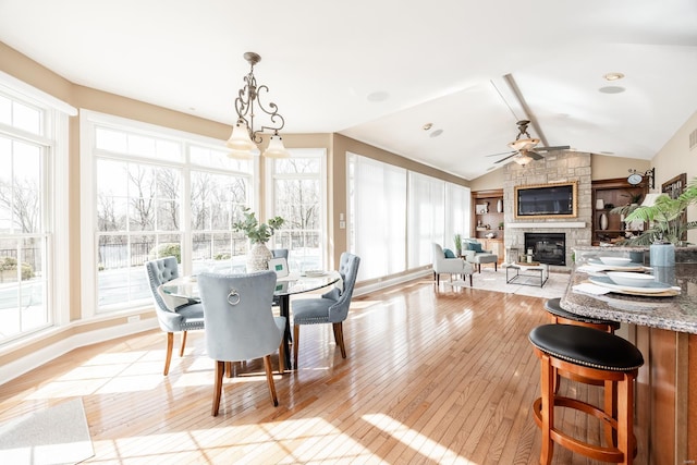 dining space featuring ceiling fan, vaulted ceiling, light wood-style flooring, a fireplace, and plenty of natural light