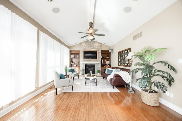 living room featuring visible vents, light wood-style flooring, a ceiling fan, a stone fireplace, and vaulted ceiling