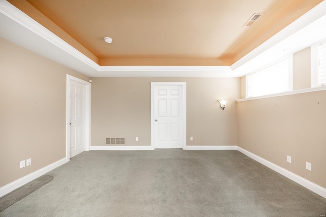 carpeted empty room featuring visible vents, a raised ceiling, and baseboards