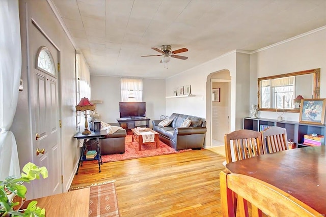 living area with arched walkways, ceiling fan, ornamental molding, and light wood-type flooring