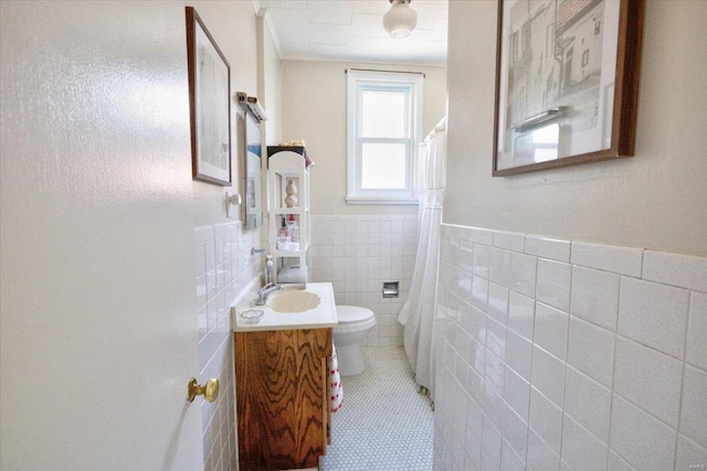 bathroom with a wainscoted wall, tile walls, toilet, vanity, and tile patterned floors