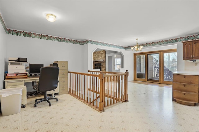 home office with arched walkways, a brick fireplace, a notable chandelier, and light floors