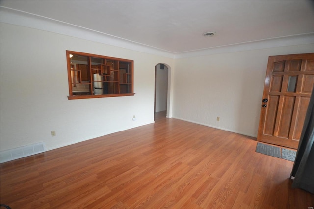 empty room featuring arched walkways, baseboards, visible vents, and light wood finished floors