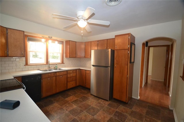 kitchen with black dishwasher, arched walkways, freestanding refrigerator, light countertops, and a sink