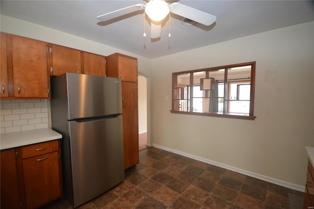 kitchen with tasteful backsplash, baseboards, brown cabinets, freestanding refrigerator, and light countertops