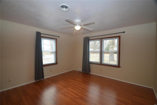 empty room with ceiling fan, wood finished floors, visible vents, and baseboards