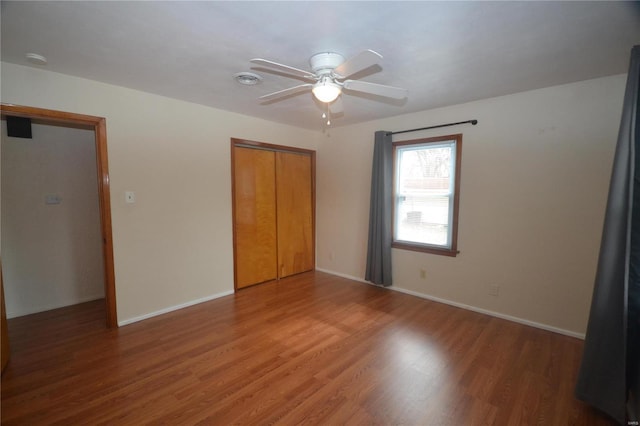 unfurnished bedroom featuring ceiling fan, a closet, wood finished floors, and baseboards