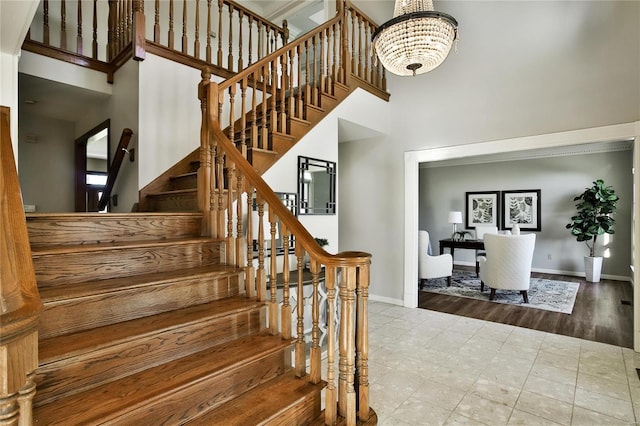 staircase featuring a towering ceiling, an inviting chandelier, and baseboards