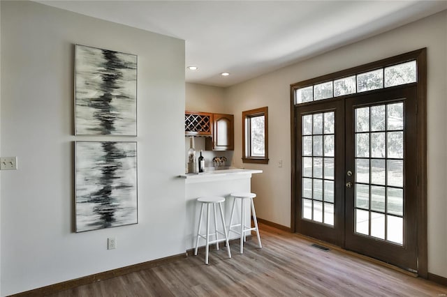 doorway to outside with french doors, a dry bar, visible vents, light wood-type flooring, and baseboards