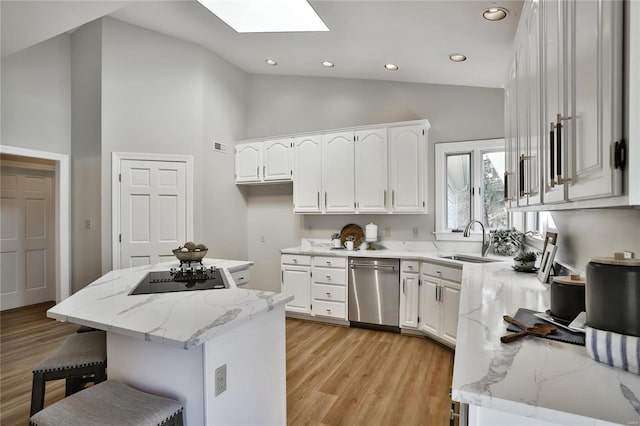 kitchen featuring a skylight, light wood-style flooring, black electric cooktop, stainless steel dishwasher, and a sink