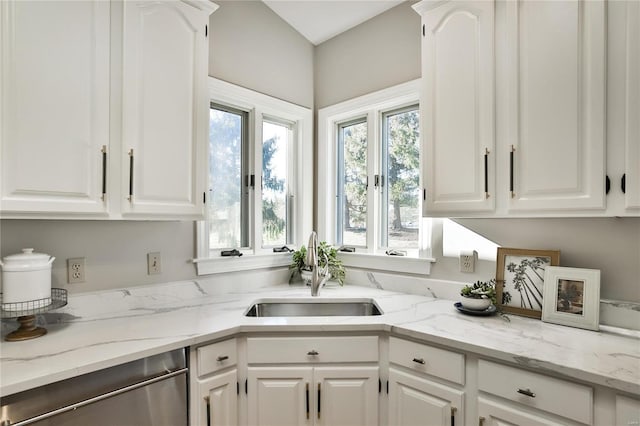 kitchen featuring stainless steel dishwasher, white cabinetry, light stone counters, and a sink