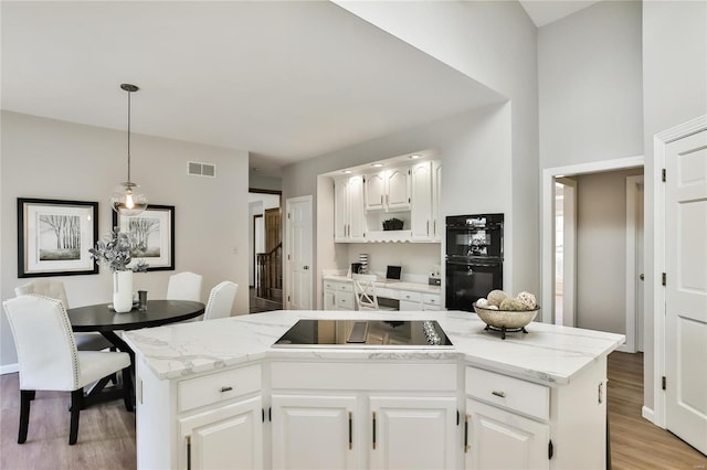 kitchen with visible vents, white cabinets, a center island, black appliances, and decorative light fixtures