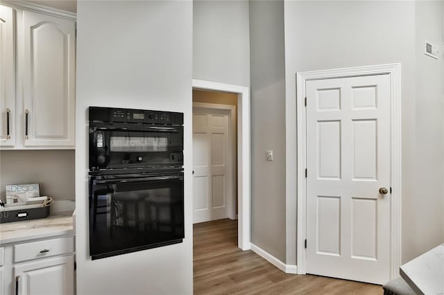 kitchen with light wood finished floors, dobule oven black, visible vents, white cabinets, and baseboards