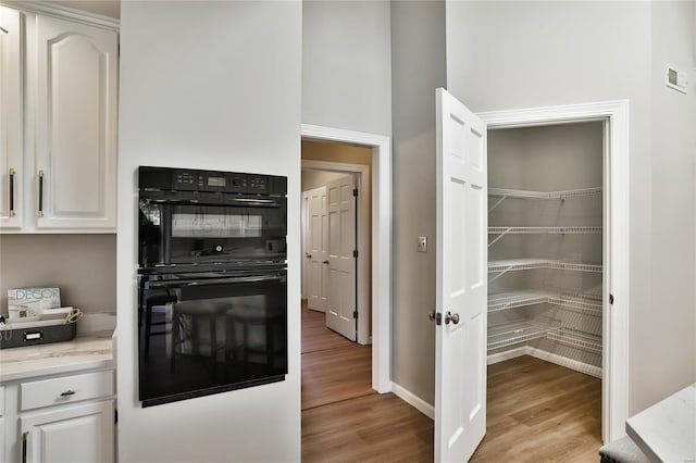 kitchen featuring light stone counters, dobule oven black, visible vents, white cabinets, and light wood-type flooring