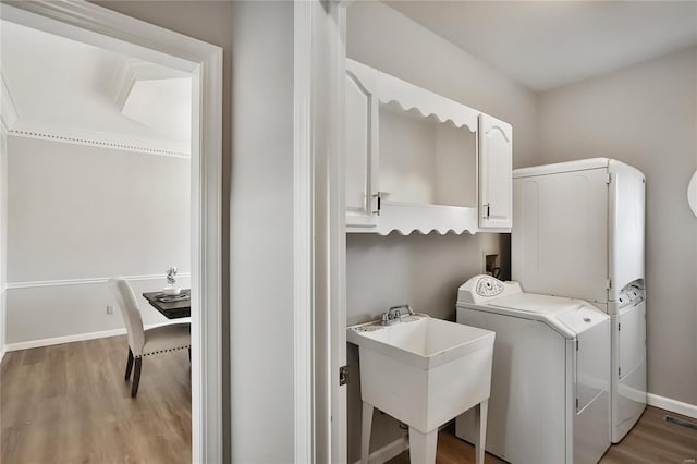 laundry room featuring cabinet space, baseboards, light wood-style floors, washing machine and dryer, and a sink