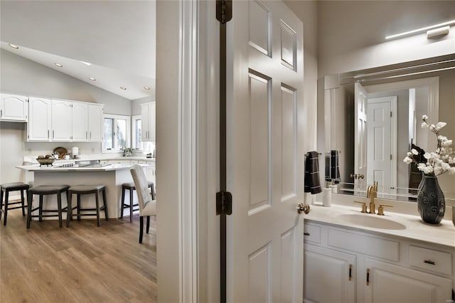 bathroom with lofted ceiling, vanity, recessed lighting, and wood finished floors