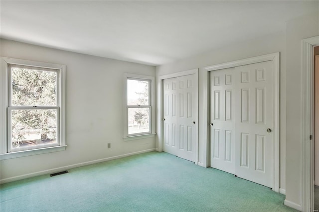 unfurnished bedroom featuring multiple closets, light colored carpet, visible vents, and baseboards