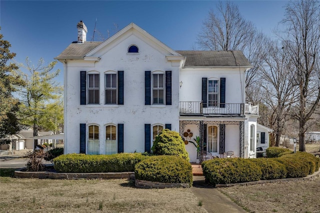 view of front of house featuring brick siding, covered porch, a chimney, and a balcony