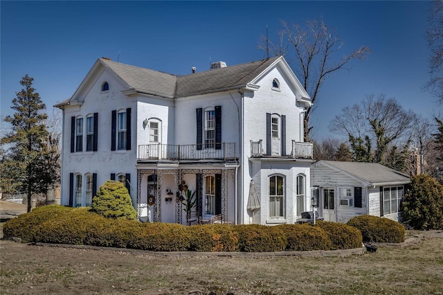 view of front of home featuring brick siding, a chimney, and a balcony