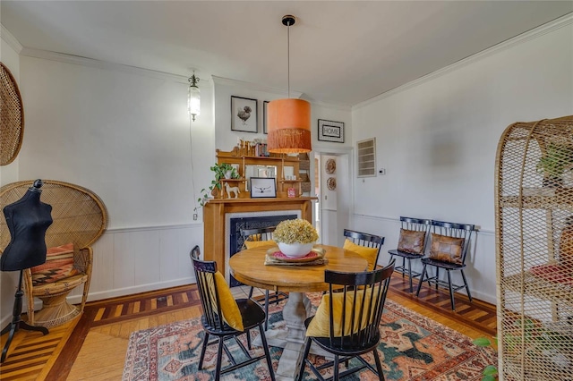 dining area with a glass covered fireplace, crown molding, wood finished floors, and wainscoting