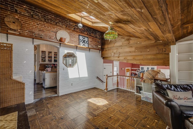 interior space featuring a towering ceiling, wooden ceiling, a skylight, and brick wall