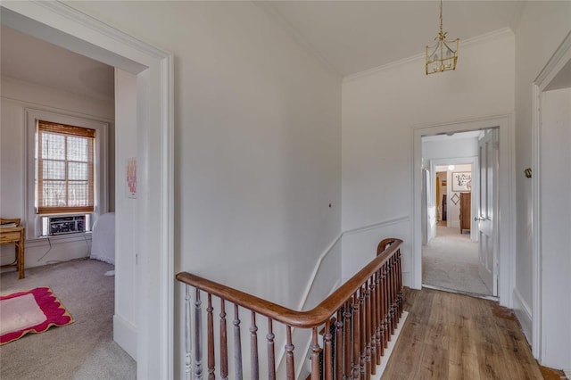 hallway with carpet flooring, wood finished floors, an upstairs landing, and ornamental molding