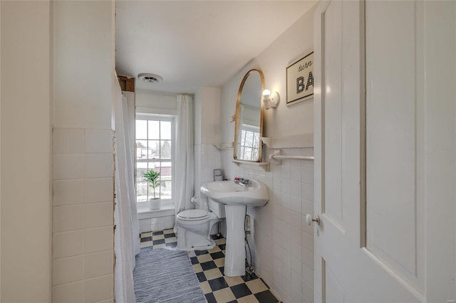 bathroom with a wainscoted wall, visible vents, tile patterned floors, toilet, and tile walls