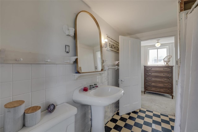 bathroom with a wainscoted wall, a sink, tile patterned floors, toilet, and tile walls